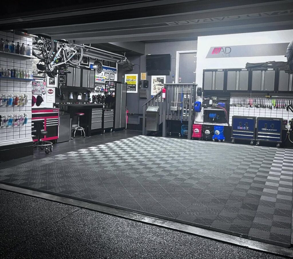 Organized garage workshop featuring checkered floor mats, metal tool cabinets, and wall-mounted storage shelving.