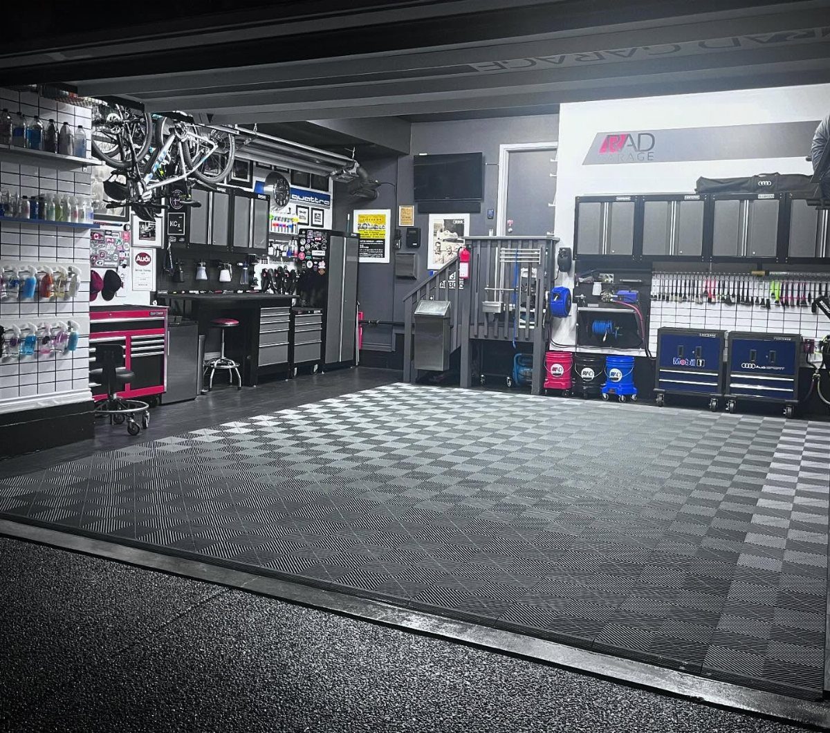 Organized garage workshop featuring checkered floor mats, metal tool cabinets, and wall-mounted storage shelving.