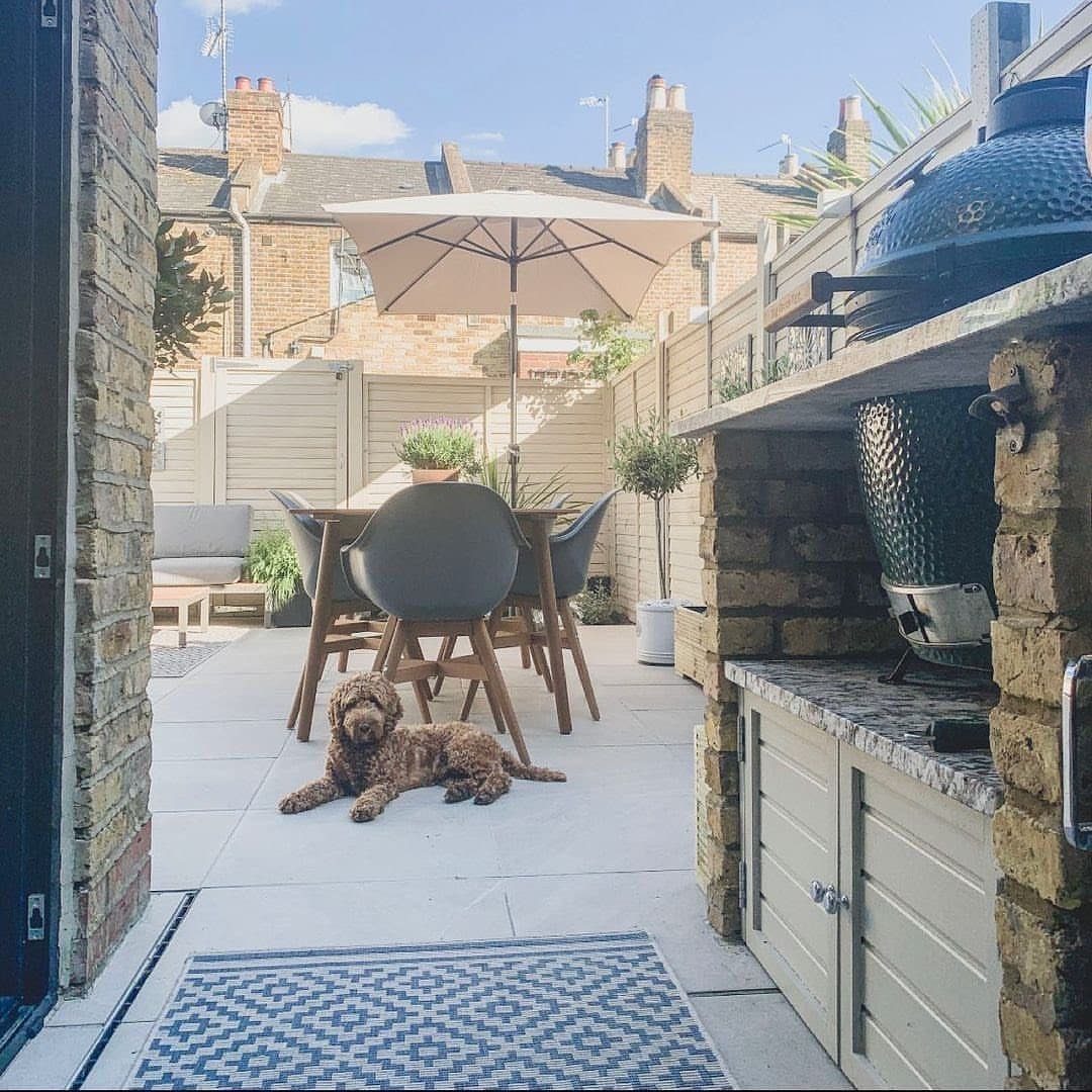 A modern patio with outdoor dining furniture, a built-in grill, and a dog lying on the tiles.