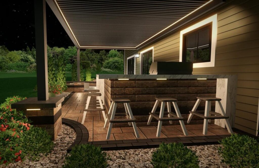 Modern outdoor kitchen with a stone bar, white stools, and a slatted pergola at night.