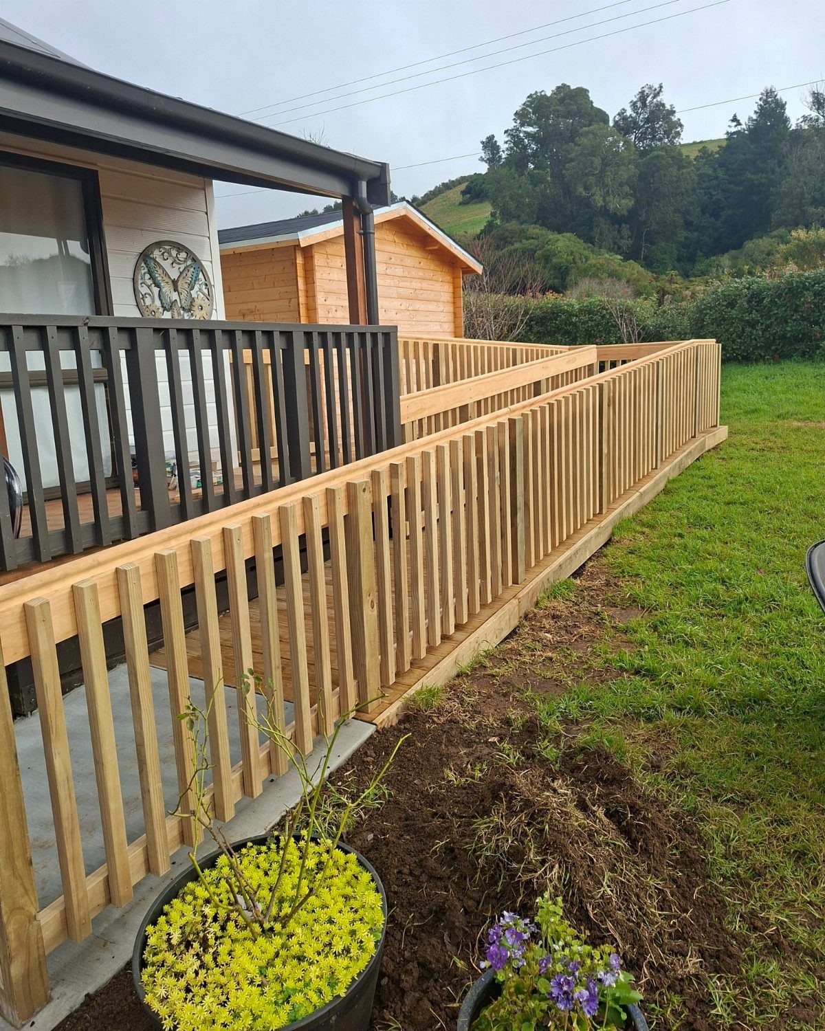 A long wooden deck with light timber railings running alongside a house and a green lawn.
