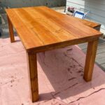 A simple rectangular wooden outdoor dining table resting on a pink drop cloth.
