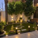 Small landscaped garden with bollard lights and ground lighting illuminating green grass and shrubs.