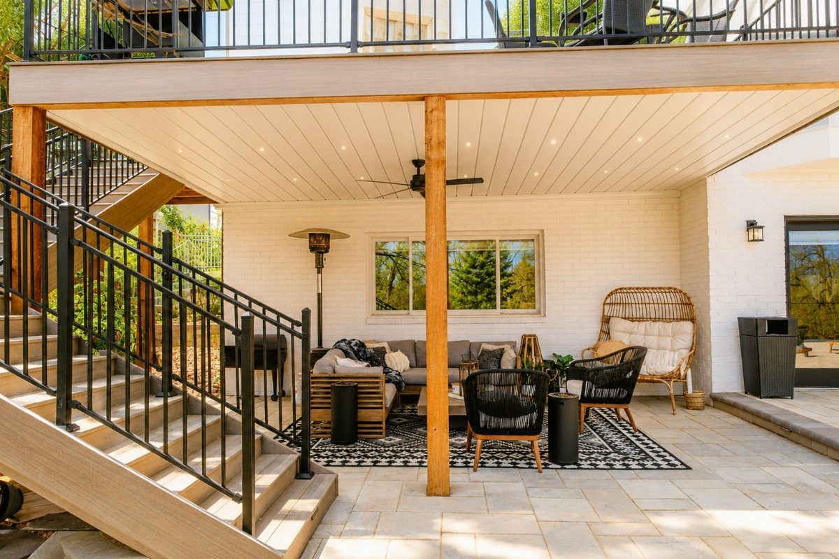 Outdoor living room furniture set on a stone patio under a wooden deck ceiling.