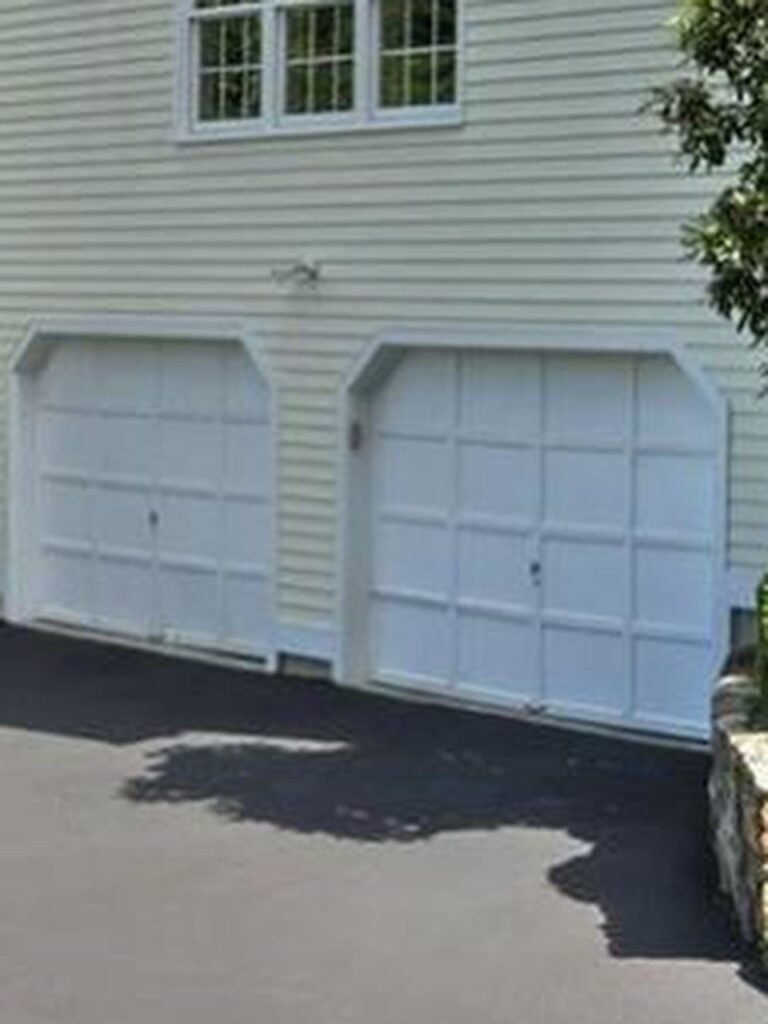 Two white paneled garage doors on a light yellow house with an asphalt driveway.