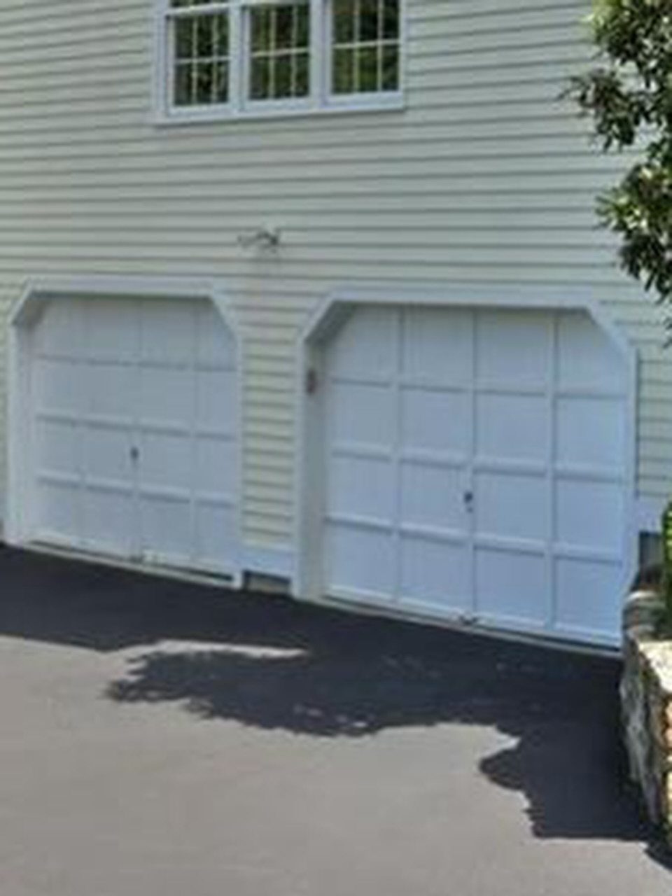 Two white paneled garage doors on a light yellow house with an asphalt driveway.