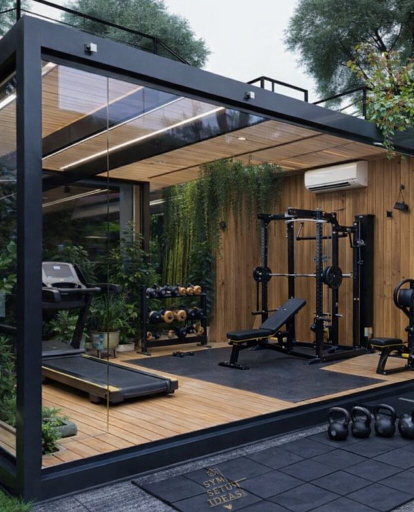 Modern glass-walled backyard gym shed containing a treadmill, weight rack, and squat rack on wooden flooring.
